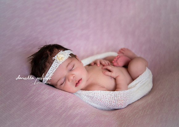 baby girl wrapped in white sleeping on a pink blush blanket