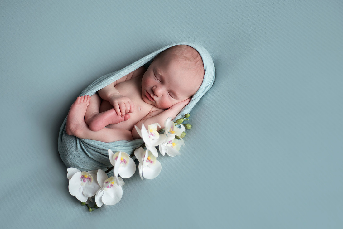 Newborn baby boy with dark hair cocooned in a wrap smiling as he dreams